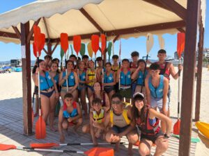 Jóvenes practicando kayak en Hemojuve 2026 Imagen de los participantes Hemojuve 2026 en la playa bajo una carpa, sosteniendo los remos de la actividad de kayak